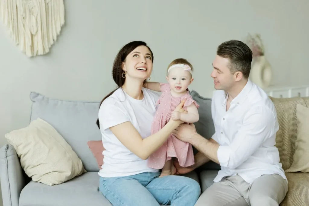 Family sitting together on a living room couch with a baby, enjoying time at home in a bright, comfortable space.