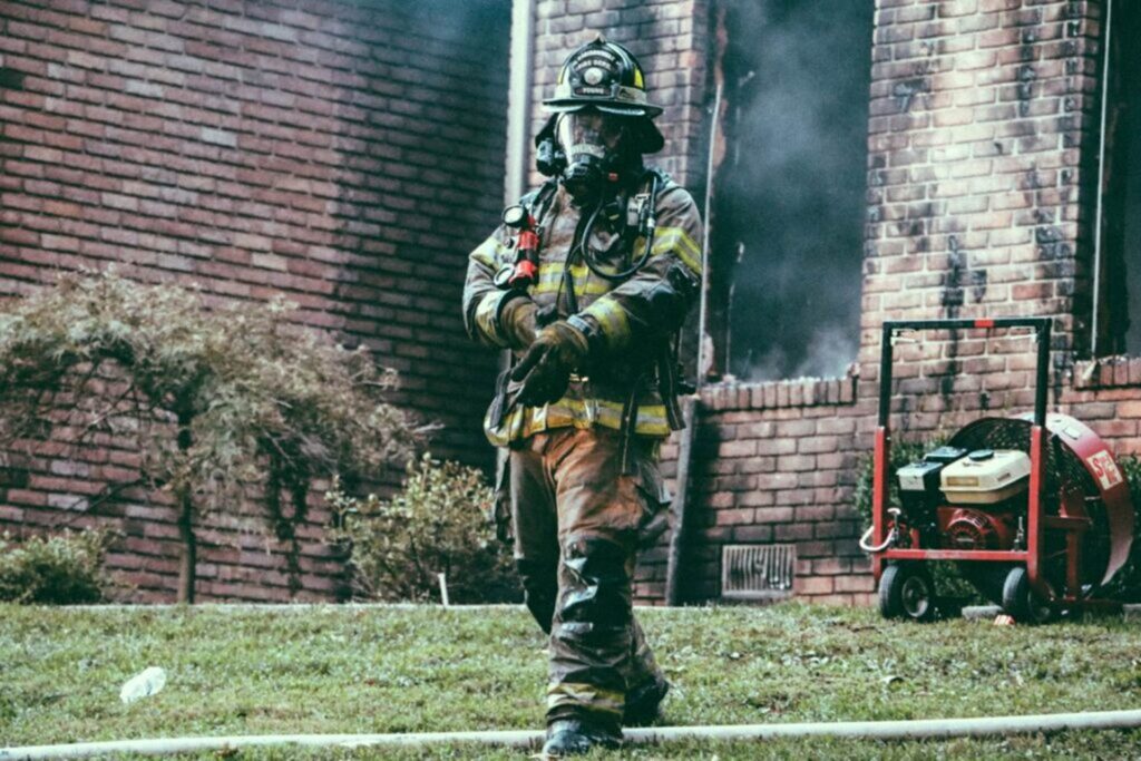 Firefighter wearing breathing apparatus outside a brick building with smoke visible from windows during emergency fire response.