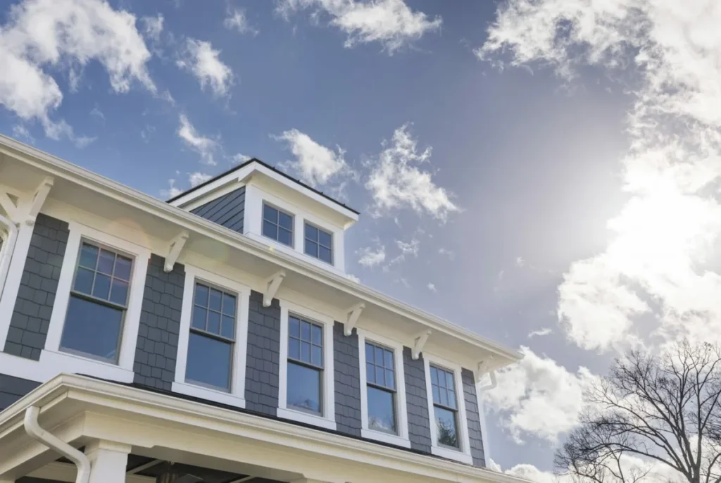 Two-story house with blue siding and white trim under a sunny sky with scattered clouds.