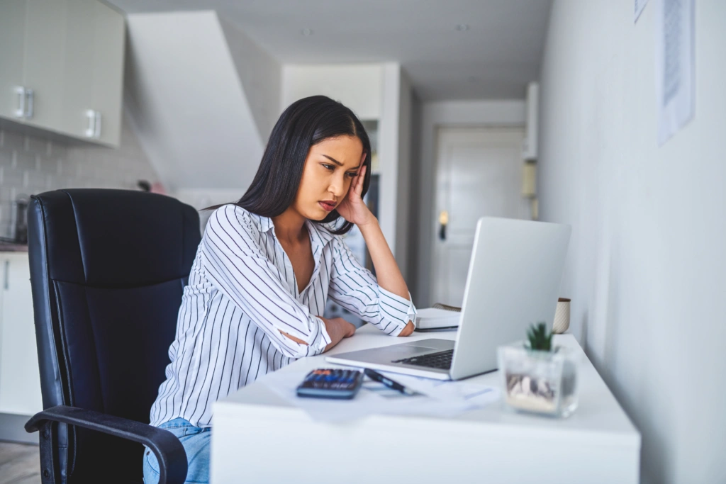 Person working at a home office desk, reviewing financial documents and a laptop beside a calculator.