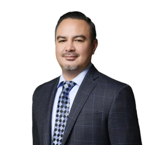 Danny Coronado - WBG - 500x500 Danny Coronado professional headshot wearing a patterned dark suit jacket, light blue dress shirt, and geometric-patterned tie against a light gray background.