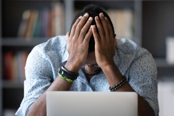 Person sitting at a laptop with hands covering their head, illustrating financial stress, debt concerns, or budgeting challenges.