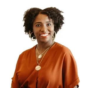 Shimene Willard - WBG - 500x500 Shimene Willard professional headshot wearing a rust-colored blouse and layered necklaces against a light neutral background.
