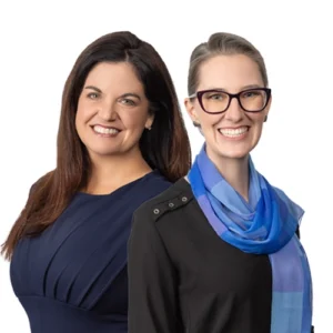 Team Kim - WBG - 500x500 Team Kim professional headshot featuring two women standing side by side, one in a navy dress and one wearing glasses with a blue scarf, against a light gray background.