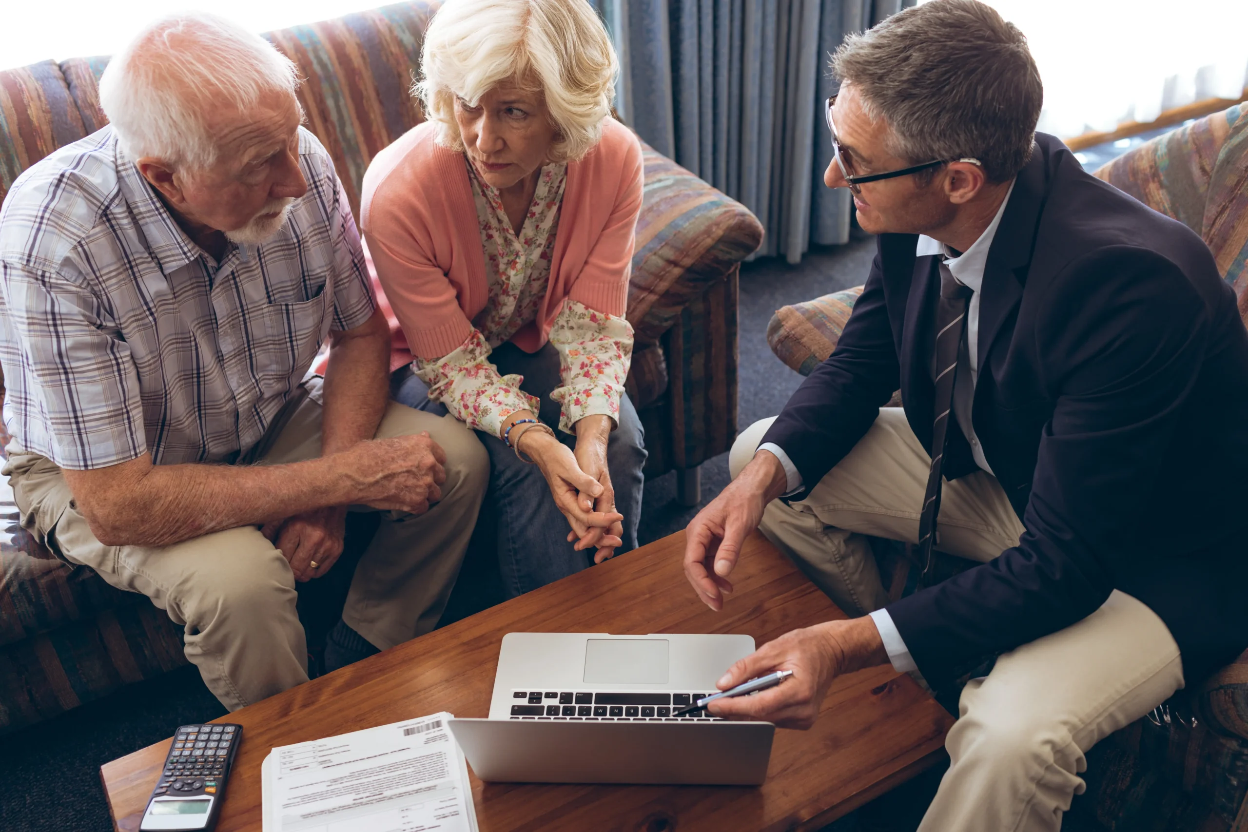Financial advisor meeting with older homeowners at home, reviewing financial planning documents and information on a laptop.